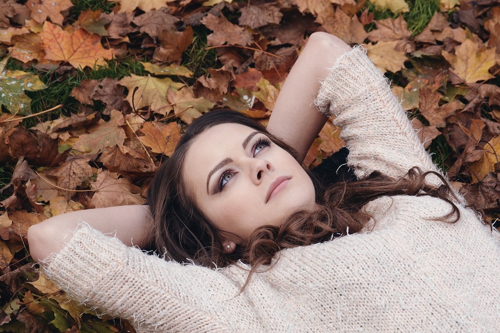 落ち葉の上で仰向けに寝転んでいる女性の画像